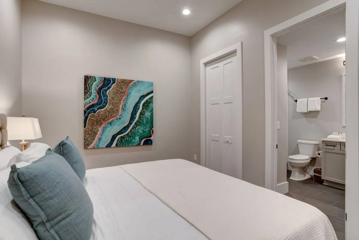 A peaceful king bedroom with a richly dressed bed, soft pillows, tasteful artwork, and a doorway leading to a private bathroom. Soft morning light filters into the space, enhancing the sense of restful seclusion and privacy.