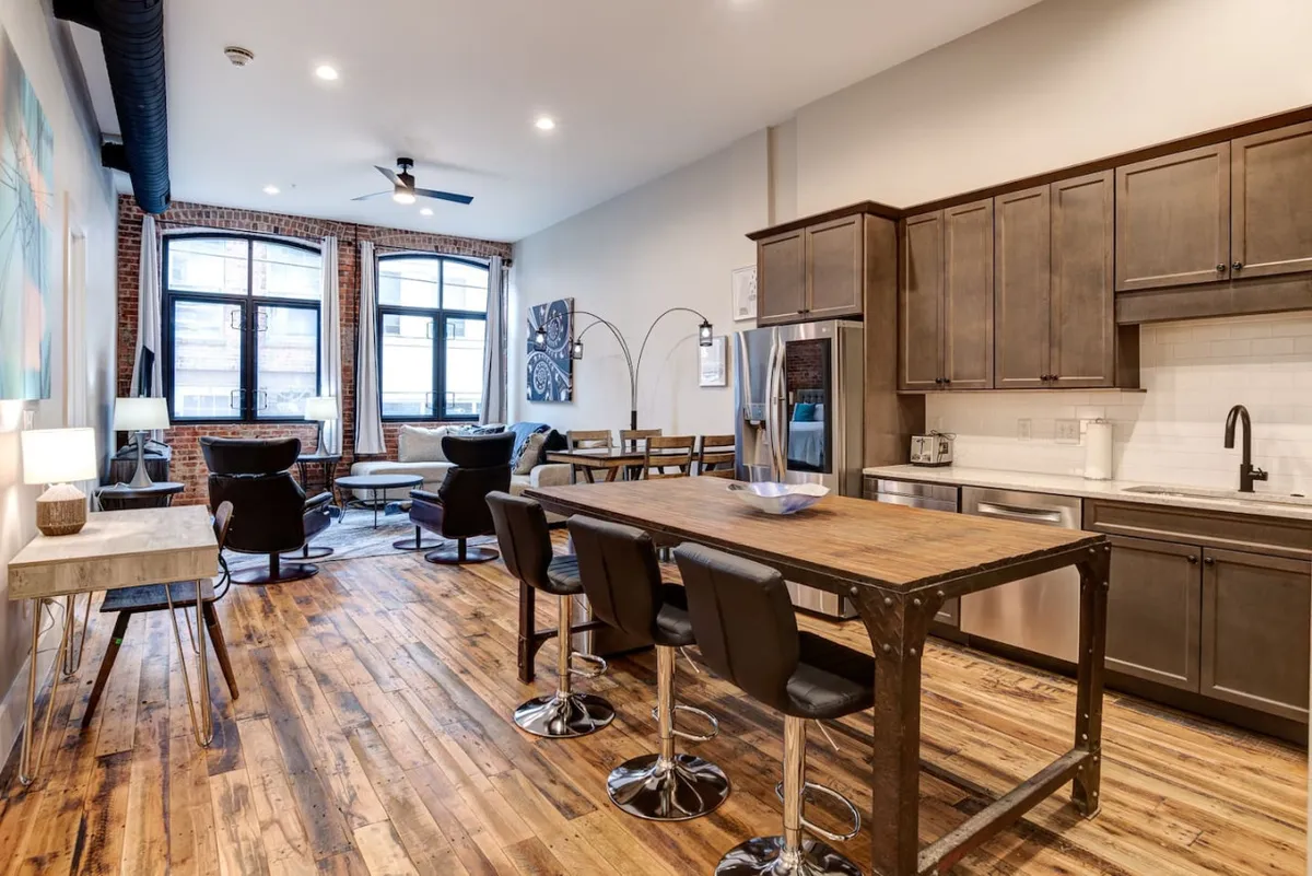 A sunlit kitchen and dining area featuring a spacious island, comfortable seating, and large windows that bathe the space in natural light. The modern furnishings and open design promote a seamless transition from cooking to dining and lounging, making it ideal for both everyday meals and special occasions.