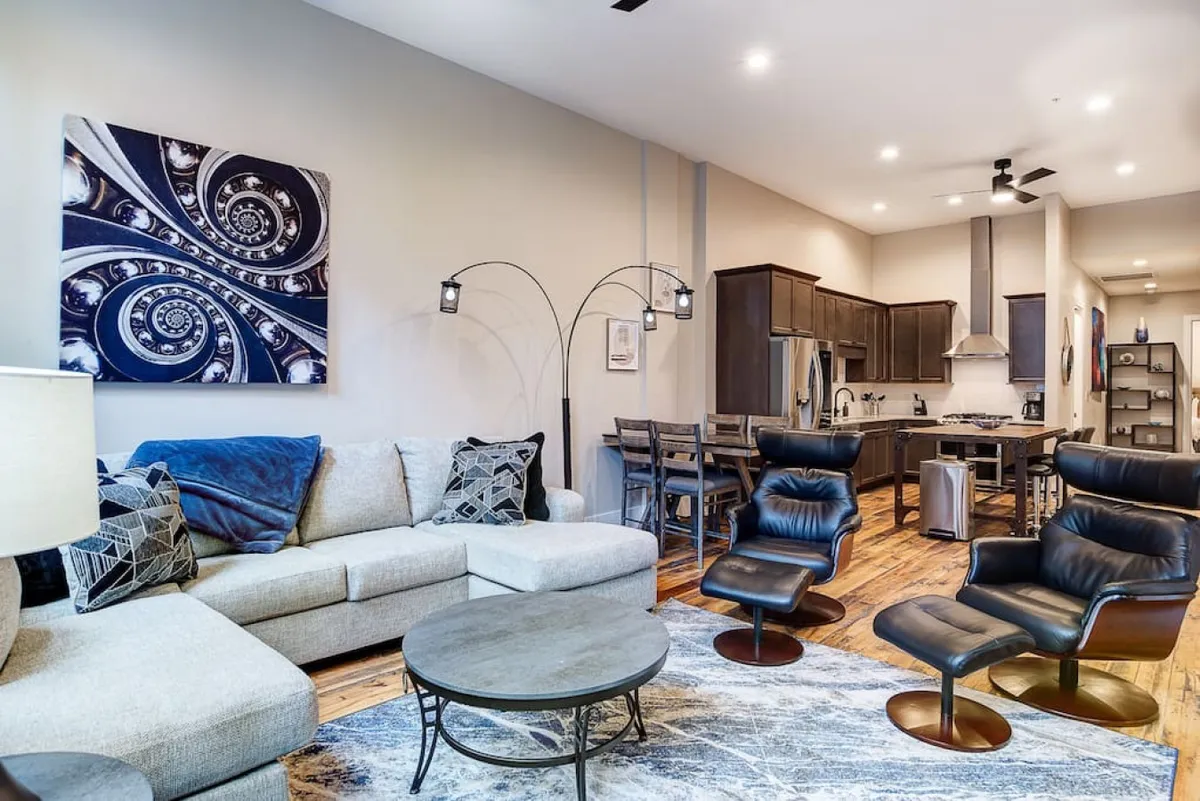 A modern open-concept living and dining area with a comfortable sofa, vibrant artwork, and a dining table seamlessly connected to the kitchen. The layout encourages easy flow for entertaining or relaxing, while colorful decor and thoughtful details add a contemporary touch.
