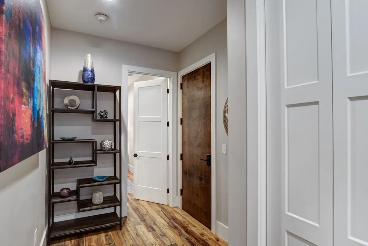 This image captures an inviting entryway, with colorful artwork displayed on the walls and an open doorway leading further into the home. Decorative shelving adds both style and function, and guests are seen admiring the vibrant art as they enter, setting a tone of warmth and welcome.