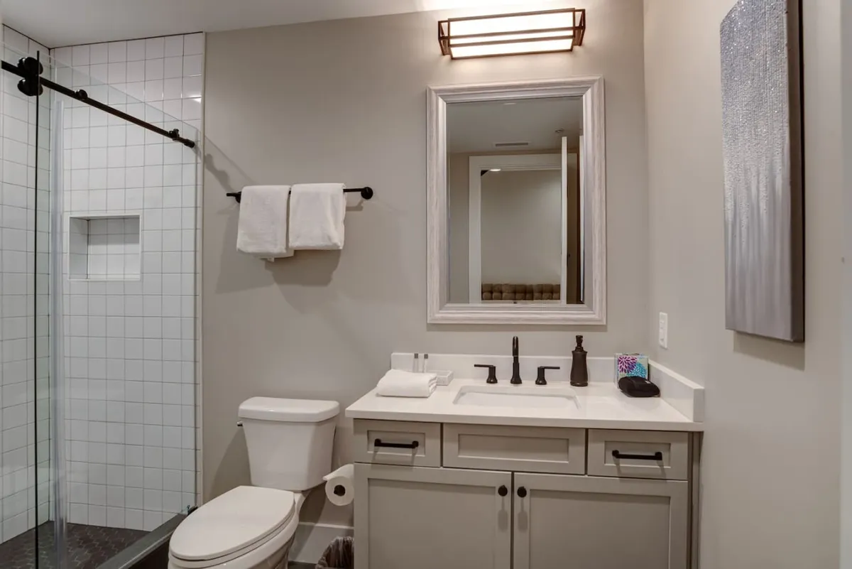 A thoughtfully designed half-bath featuring a sleek vanity, well-lit mirror, and plush towels. The contemporary fixtures and calming hues provide a practical yet stylish touch for guests and groups.