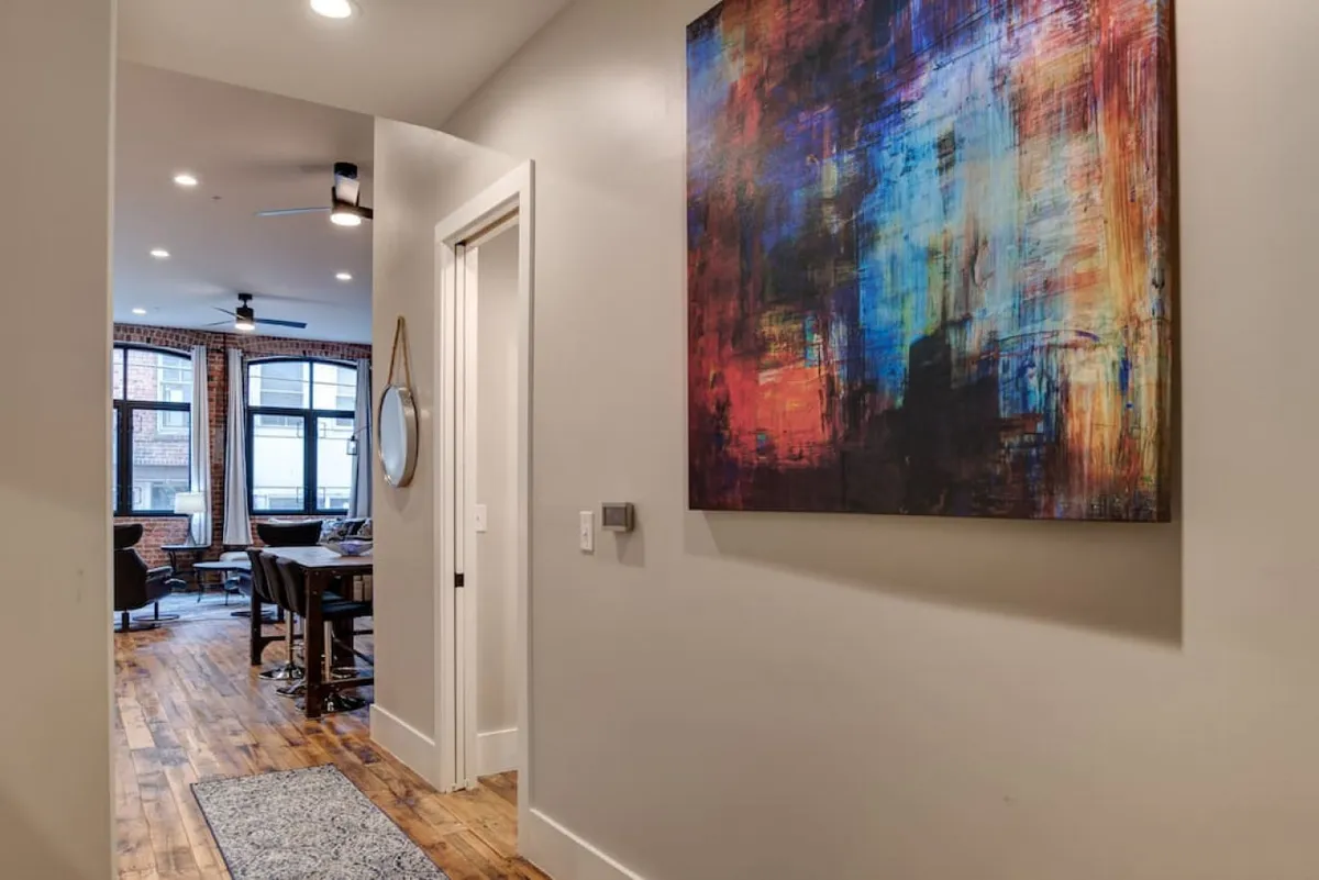 Looking beyond the hallway, this image features a colorful abstract painting and mirrored wall décor, with an open living space visible in the background. The area is bathed in natural light, creating a lively, modern atmosphere that hints at the downtown energy just outside.