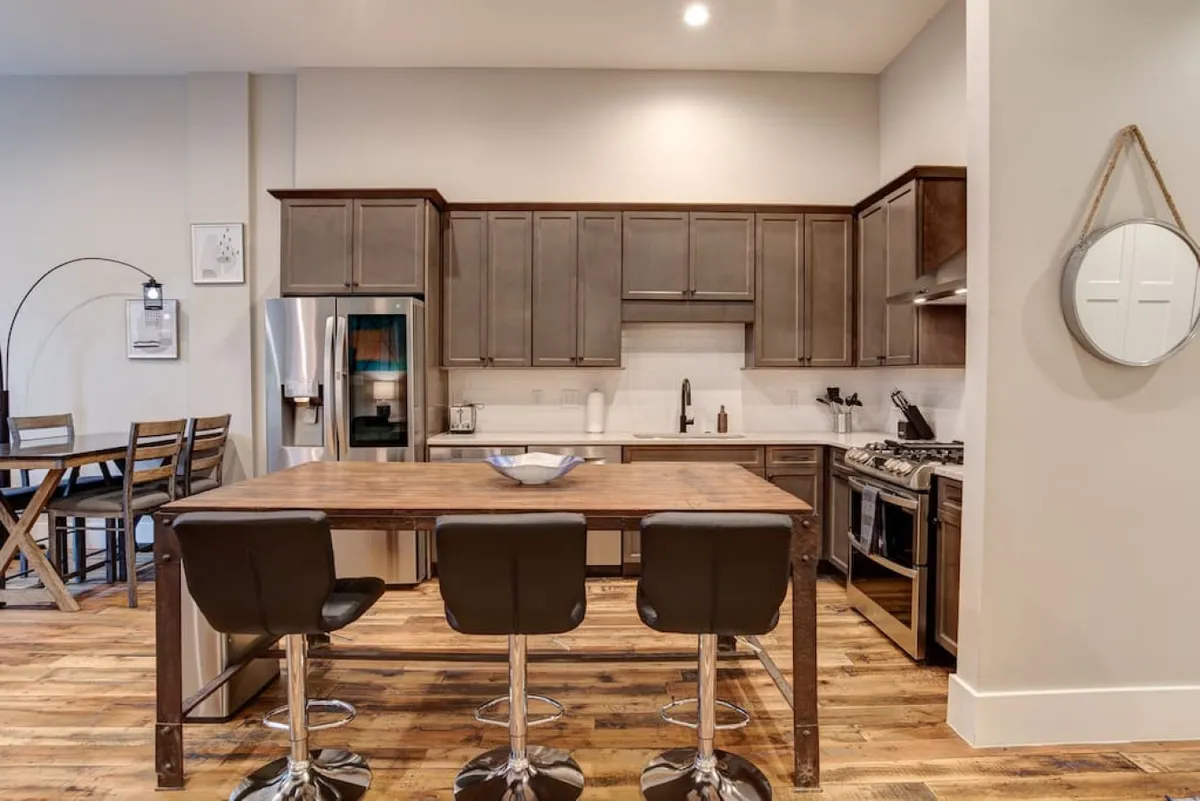 A bright, contemporary kitchen featuring a generous kitchen island perfect for food prep or casual gatherings. Stainless steel appliances provide a sleek, modern look, while the adjacent dining table suggests a seamless flow for shared meals and socializing. The overall mood is both cozy and modern, with details that blend functionality and warmth.